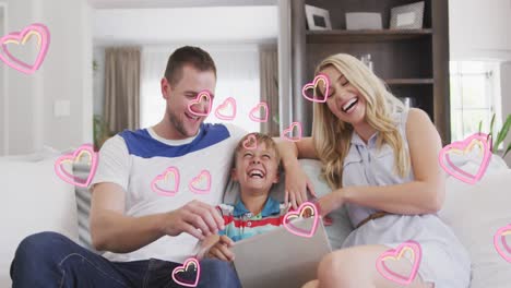 Animation-of-hearts-over-happy-caucasian-family-using-tablet-on-sofa