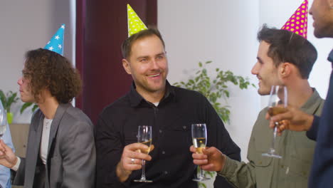 happy multiethnic group of male colleagues holding champagne glass and talking together during a party at the office