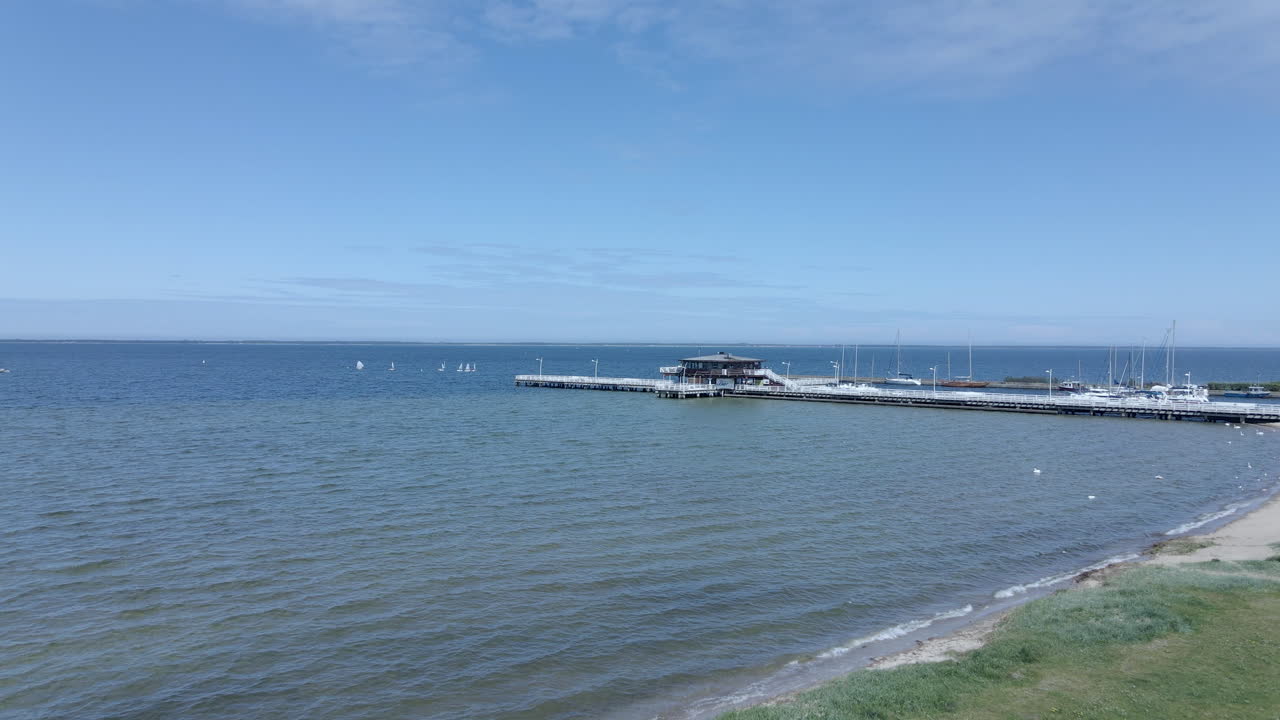 Aerial view over sea coast, in the distance a wooden pier on the water, a restaurant on the water