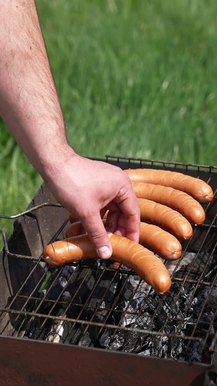 Sausages roasting on barbecue grill outdoors. Grilled food fried and smoked in charcoal grills. Man chef putting delicious sausages on a grill grate. Food for picnic. Vertical video