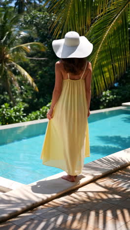 woman in a yellow dress and hat by a tropical pool