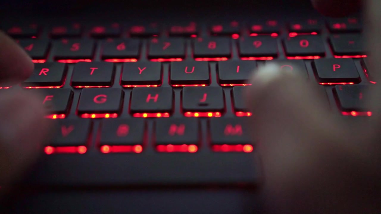 Fingers typing on red backlit keyboard, macro shot, computer use, coding, and online communication scene.