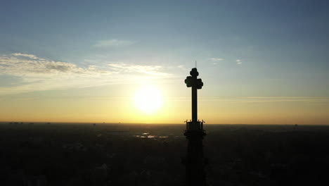 una toma aérea del campanario de una catedral con una cruz en la parte superior, tomada al amanecer