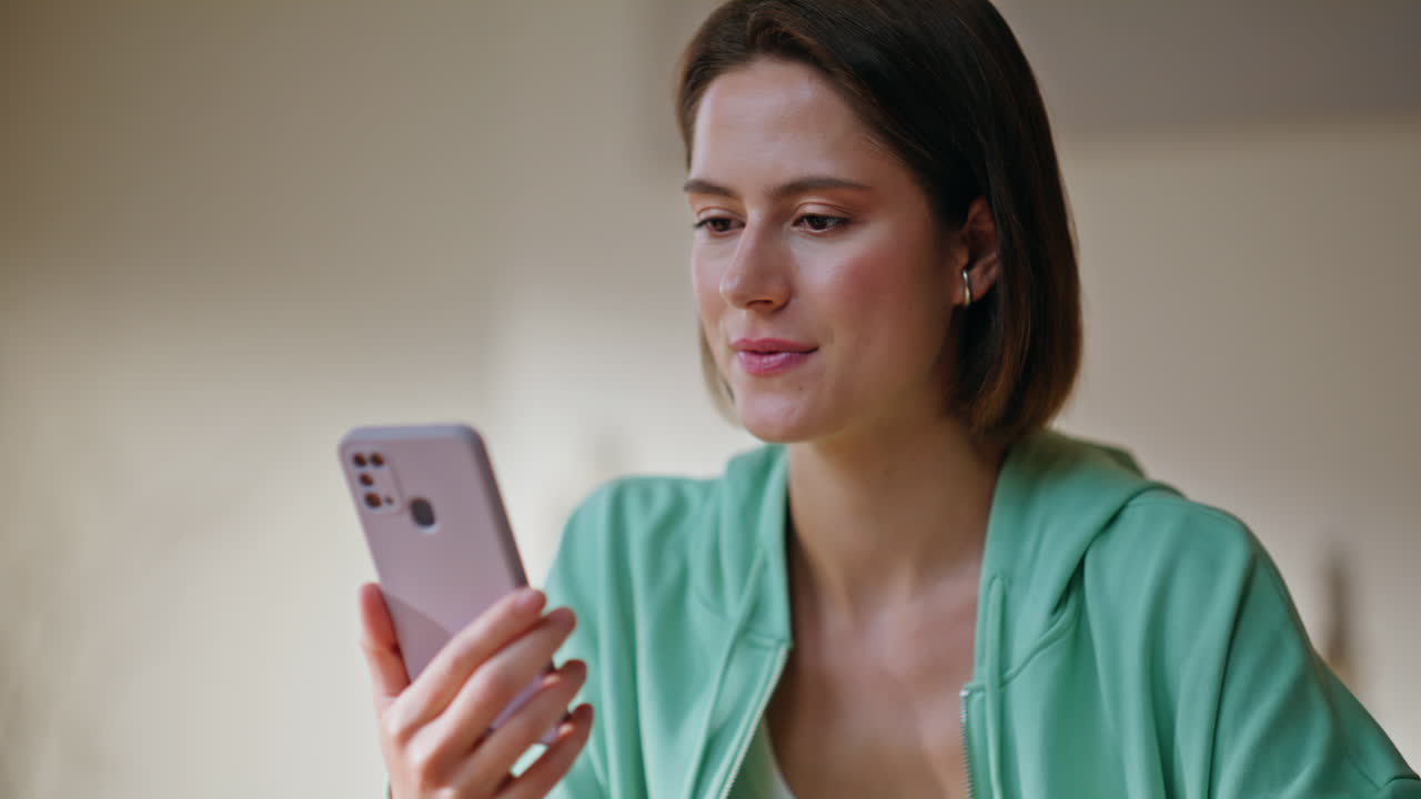 Cheerful girl reading smartphone message sitting modern apartment room closeup