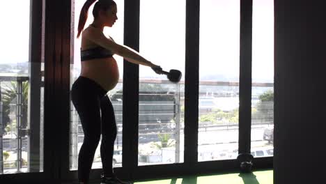 imágenes de vídeo de una modelo de fitness femenina embarazada haciendo ejercicios con pesas rusas en un gimnasio durante su tercer trimestre de embarazo.