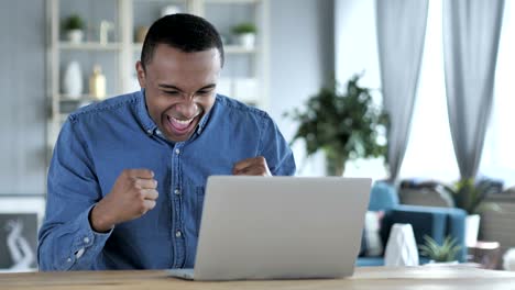 excited young african man celebrating success, working on laptop