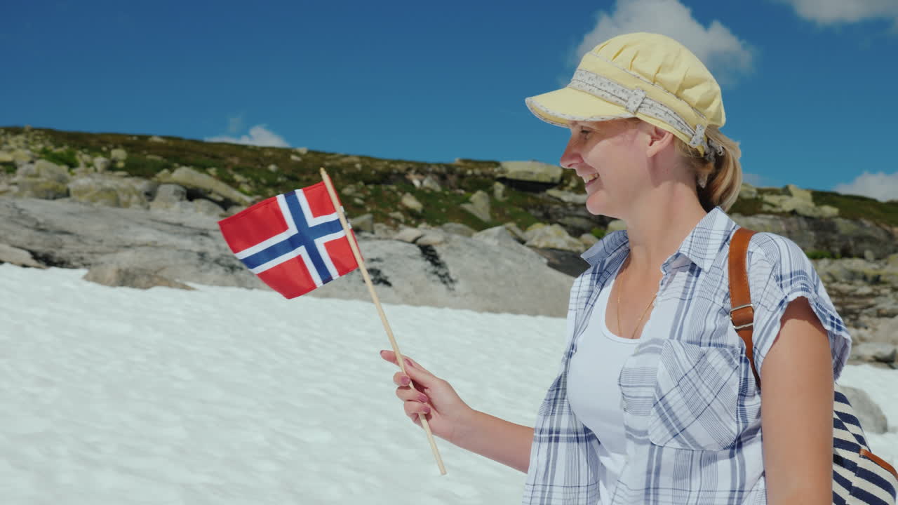 눈 덮인 피크 여름에 노르웨이 국기를 가진 여자 눈이 아직 녹지 않았습니다 관광 및 여행