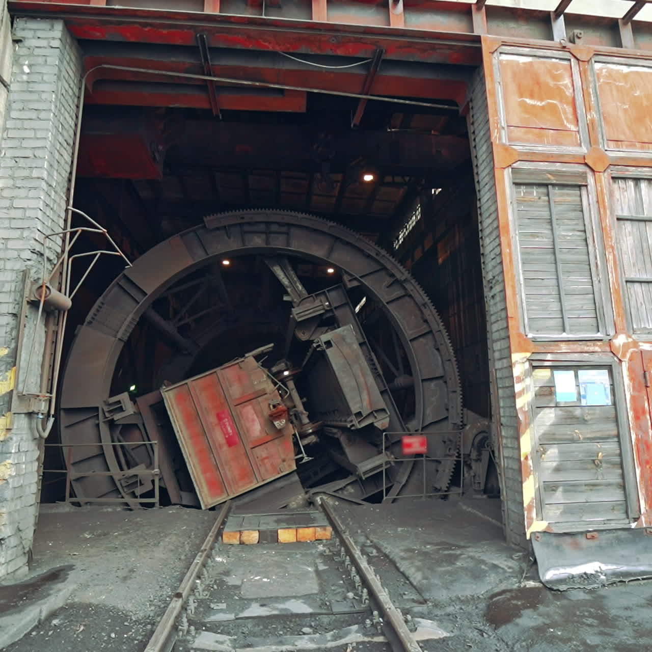 Device for unloading coal from wagon with a deaf body is rotating in the room of factory. Wagon tipper. Camera motion to back. Close-up.