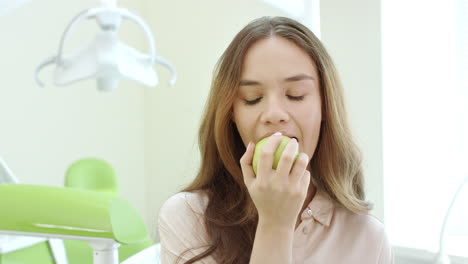 mujer feliz comiendo manzana en la clínica dental. paciente sonriente en el consultorio del dentista