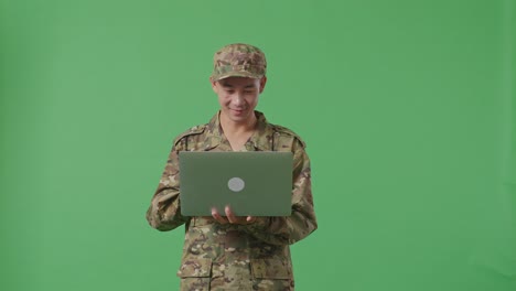 asian man soldier using a laptop and smiling while standing in the green screen background studio
