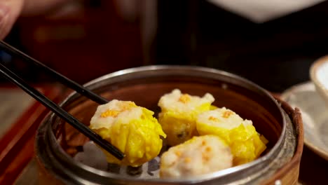 chopsticks picking dumplings from a bamboo steamer