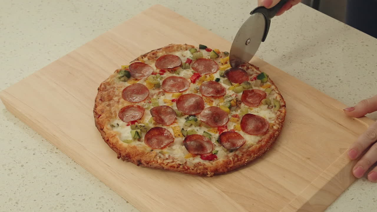 Cutting a freshly baked pizza with pepperoni and vegetables on a wooden surface