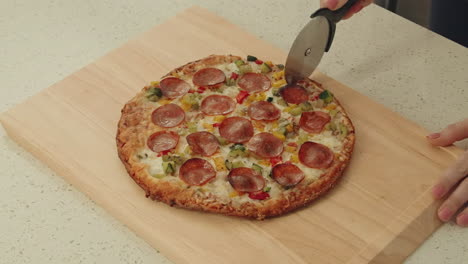 cutting a freshly baked pizza with pepperoni and vegetables on a wooden surface