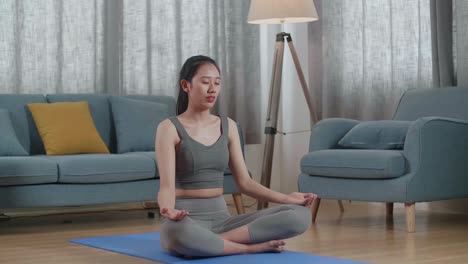 젊은 아시아 운동선수 여성이 집에서 요가 매트에서 운동하는 동안 명상합니다. 건강한 생활 방식, 피트니스, 웰빙 및 마인드풀니스