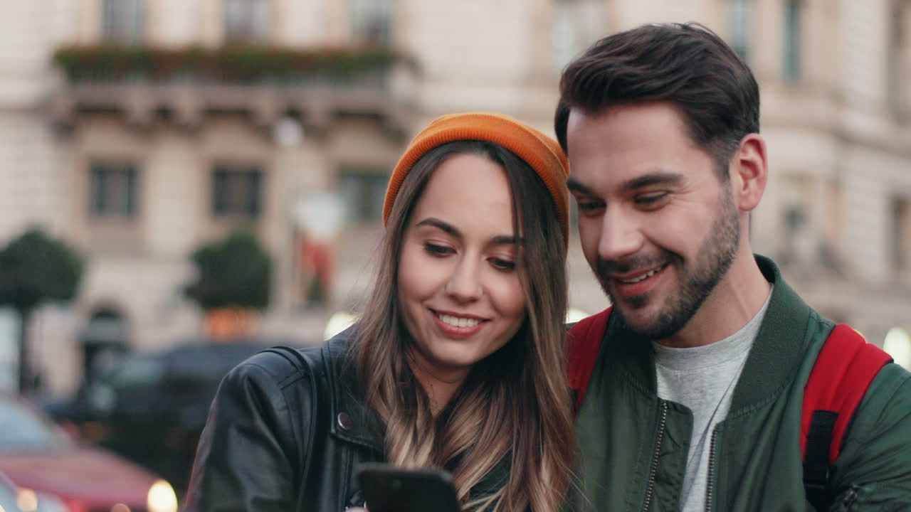 vista cercana de una pareja joven enviando mensajes de texto o jugando en el teléfono inteligente alegremente en la calle