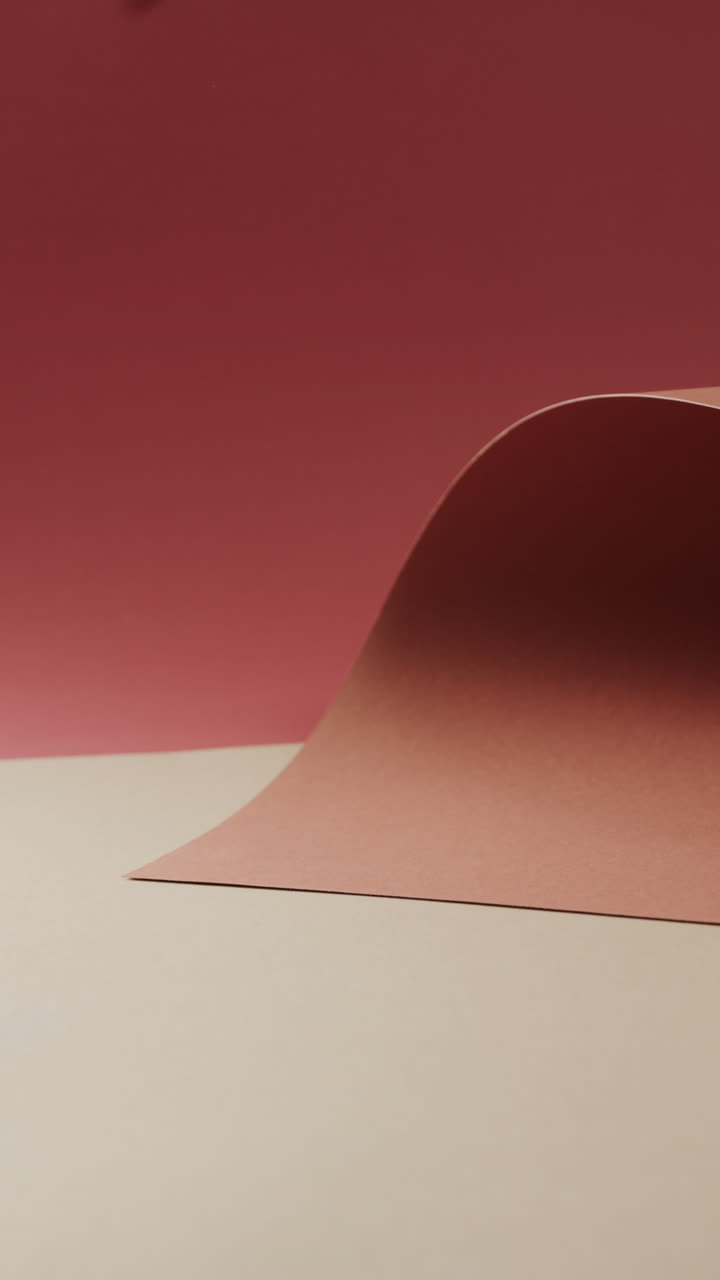 Vertical video of close up of orange and red rolled paper on beige background with copy space