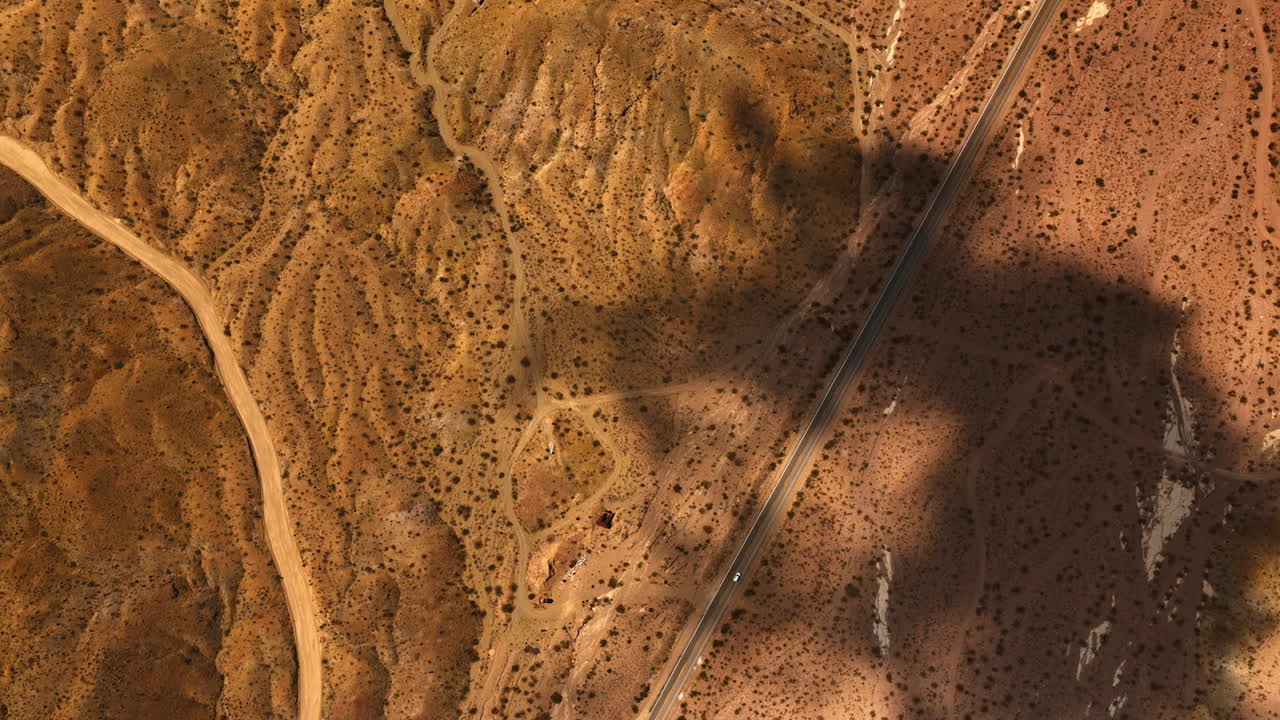 Bird's eye view on the arid desert. Dry landscape with roads and no vegetation. Mojave desert scenery with shadows from clouds.