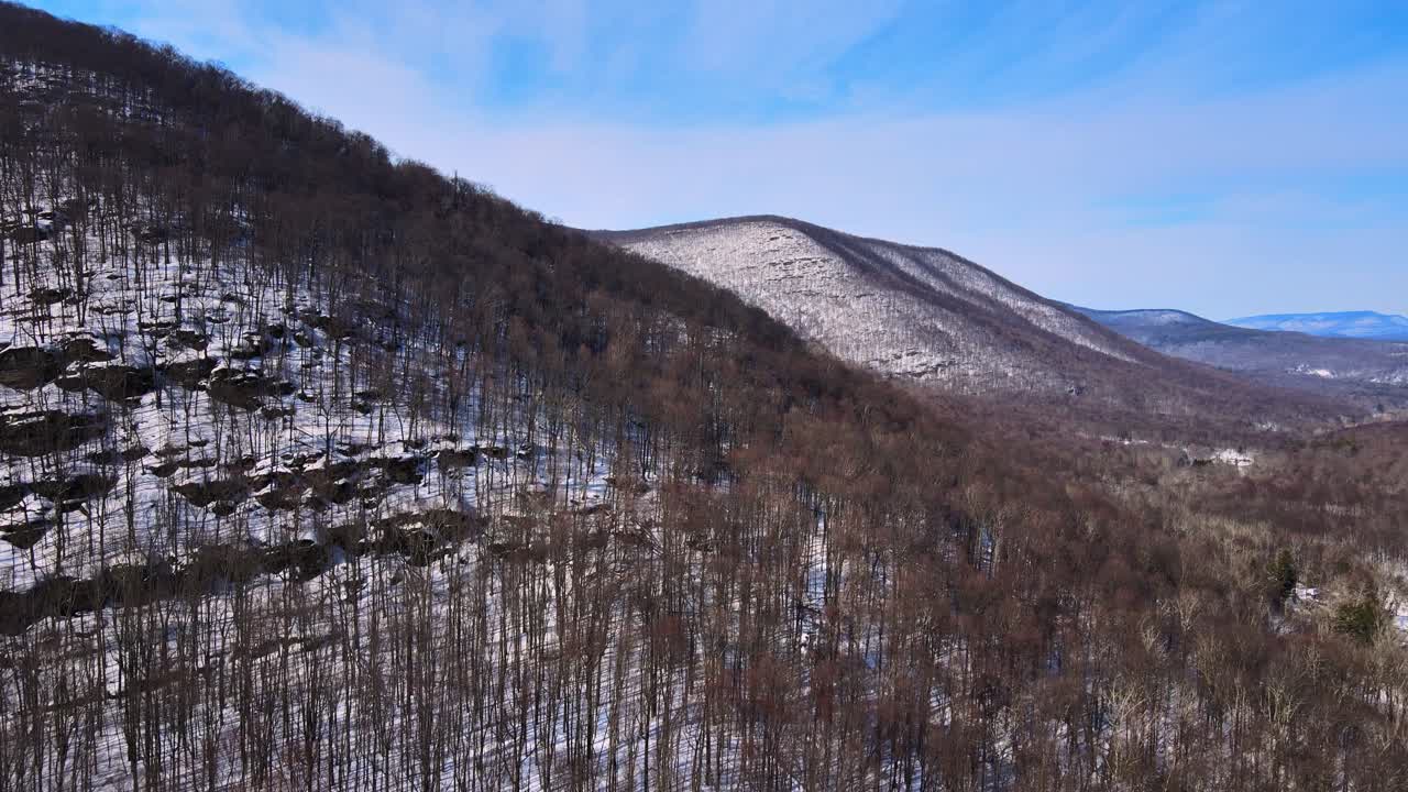 Riprese aeree con drone di una valle montana innevata all'inizio della primavera, in una giornata di sole nella catena montuosa degli Appalachi, appena dopo la fine dell'inverno, con foreste, neve, sole e cieli azzurri.