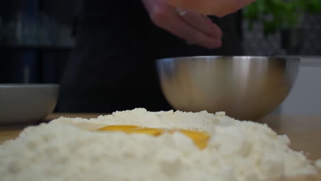 Separando-Y-Soltando-La-Yema-De-Huevo-En-Un-Montículo-De-Harina-Para-Masa-De-Pasta---Primer-Plano-Medio-A-La-Altura-De-Los-Ojos