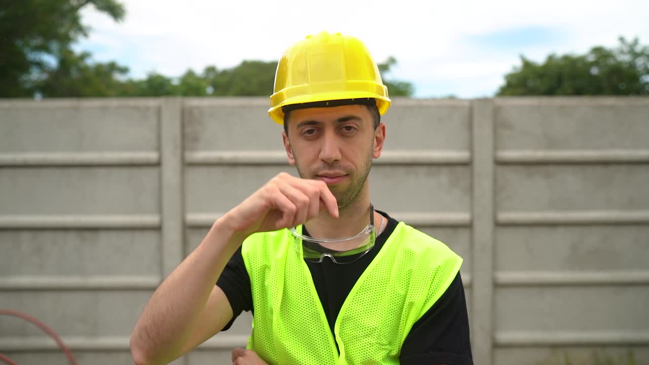un trabajador de la construcción, con un sombrero amarillo duro con gafas de seguridad estándar colocadas en su cuello, está demostrando la etiqueta adecuada del sombrero - medio de primer plano