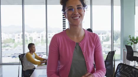 una mujer de negocios creativa de dos razas sonriente que usa una tableta en la oficina, diversos colegas en el fondo