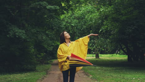 Cheerful-Woman-In-A-Raincoat-Walking-In-The-Park-And-Opening-Big-Umbrella