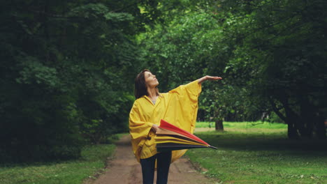 mujer alegre con un impermeable caminando por el parque y abriendo un gran paraguas