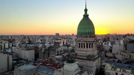 Aerial-pan-right-of-Argentine-Congress-Palace-green-bronze-dome-surrounded-by-buildings-at-sunset,-Buenos-Aires