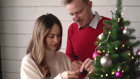 happy couple hanging christmas decoration on christmas tree at home 3