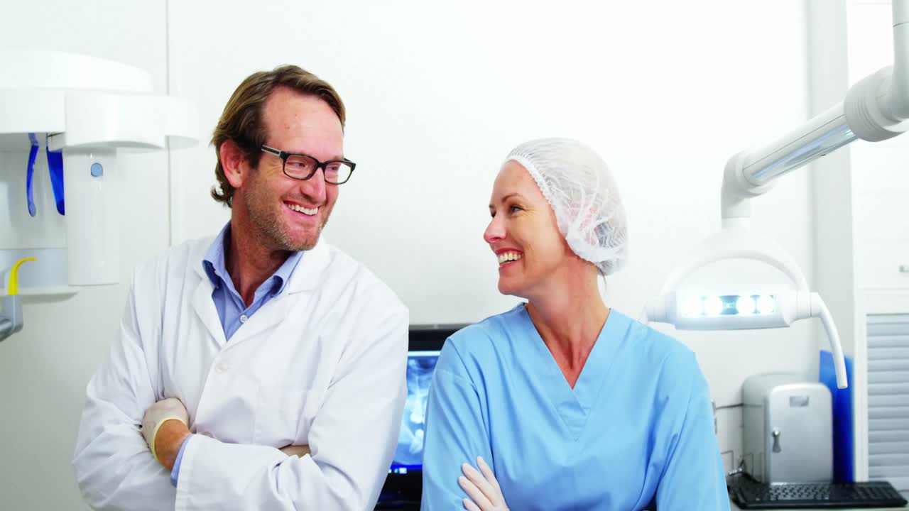 Smiling dentist and dental assistant standing with arms crossed