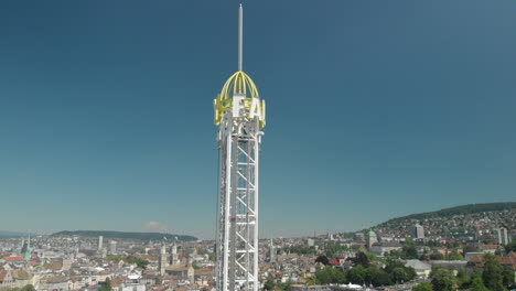 tiro de grúa de drones aéreos levantándose e inclinándose hacia abajo de la rueda de la fortuna del parque de atracciones y la torre de caída libre con la ciudad y el lago de zúrich, suiza en el fondo durante zürichfest