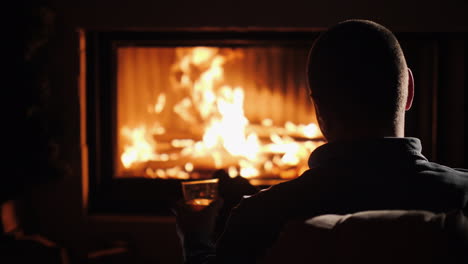 silueta de un hombre de mediana edad confiado sentado junto a la chimenea con un vaso de alcohol invierno es