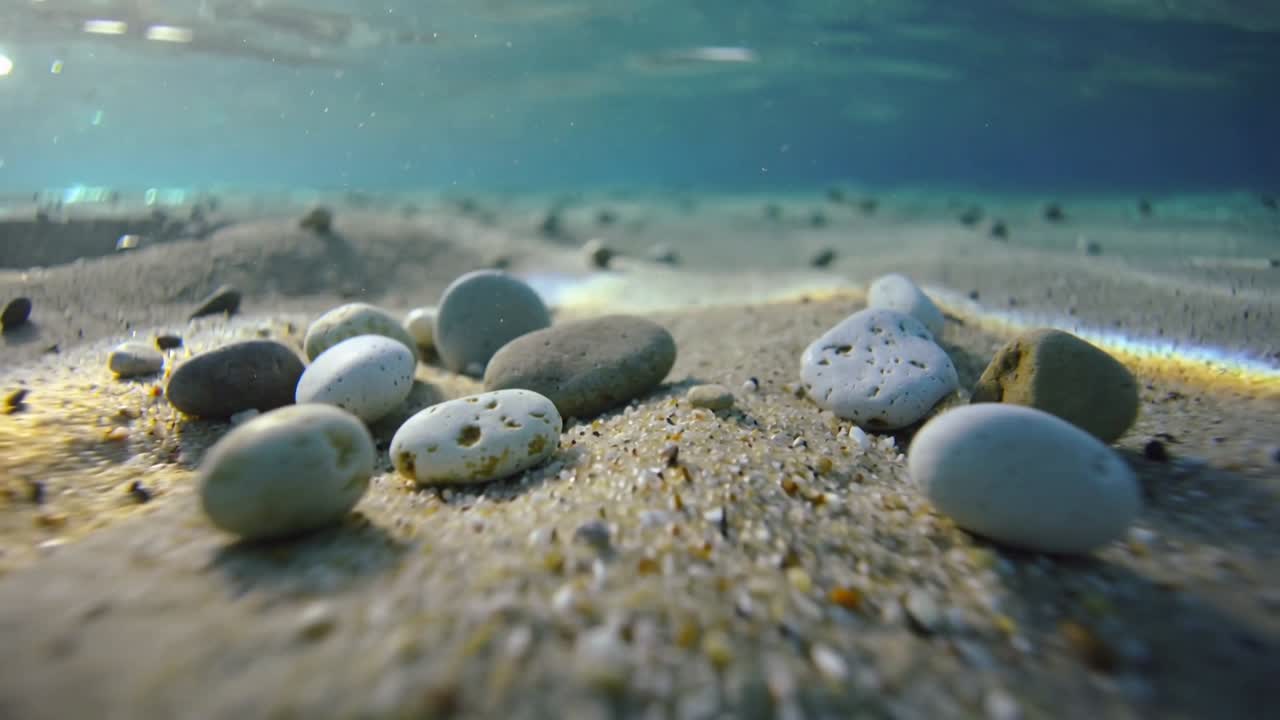 Pulling back camera revealing pebbles on rippled seabed under moving sunlit caustics to show seabed