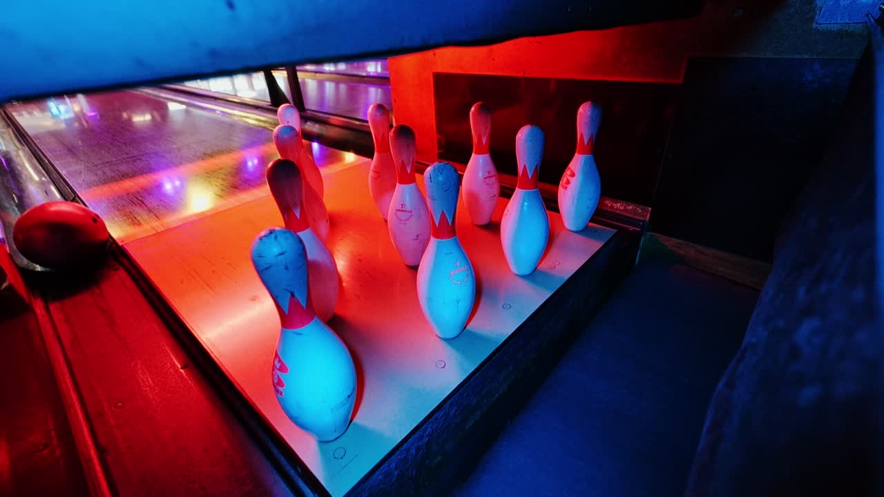 Movimento al rallentatore cinematografico di una palla da bowling che manca il bersaglio sotto luci al neon rosse e blu