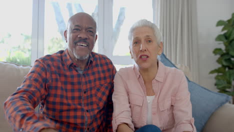 portrait of happy senior biracial couple sitting on couch having video call at home, slow motion