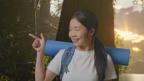 primer plano de una excursionista asiática con una mochila de montañismo sonriendo y señalando hacia un lado mientras explora la naturaleza forestal