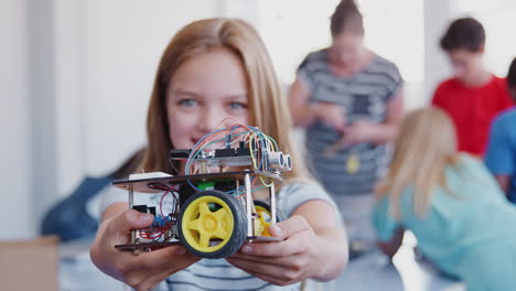 portrait of female student holding robot vehicle in after school computer coding class