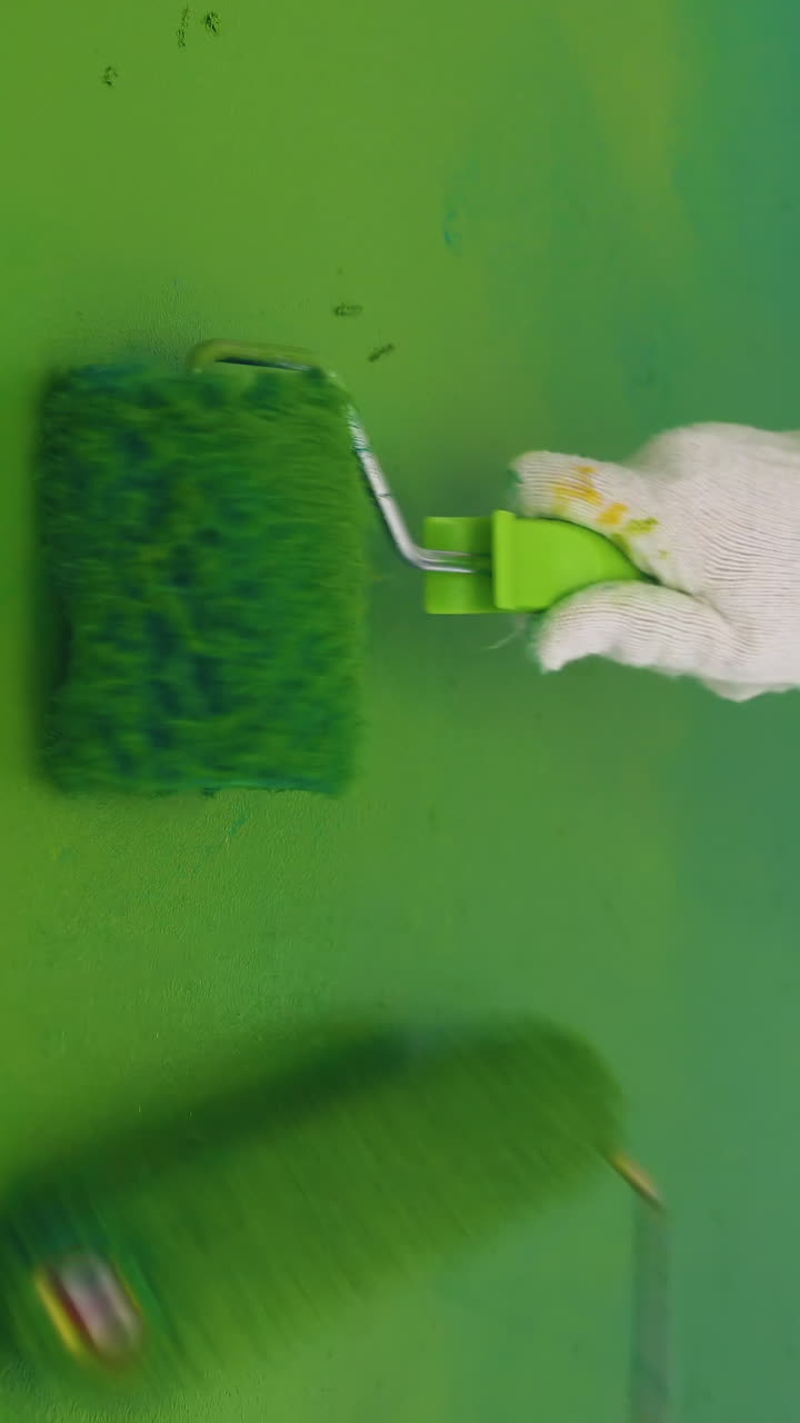 CU: skilled builders wearing white protective suits paint wall bright green color using rollers in light room close view