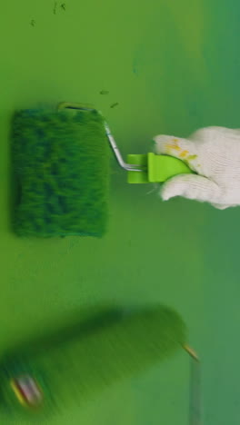 cu: skilled builders wearing white protective suits paint wall bright green color using rollers in light room close view