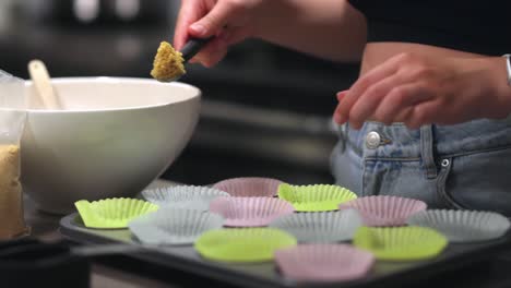 a woman is scooping and then pressing down cheesecake crumb base into a cupcake cup