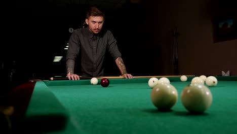 a brutal man with tattoos on his hands is playing russian billiards in a bar.