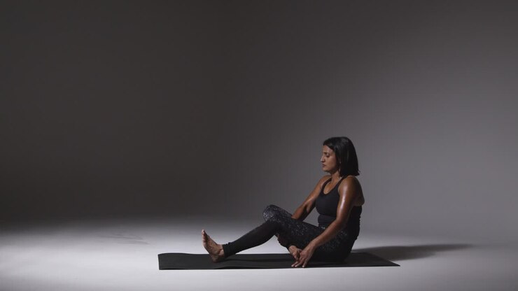 Wide Angle Studio Shot Of Mature Woman Wearing Gym Fitness Clothing Sitting On Floor Doing Pilates Stretching Exercises