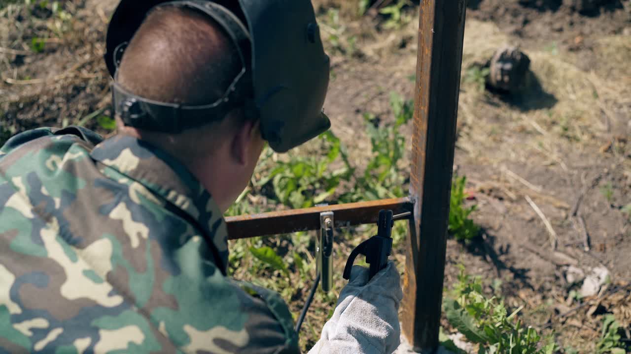 vista de atrás trabajador soldaduras y verificaciones partes metálicas de la valla