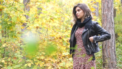 plano general de una chica morena en el bosque de otoño, se para pensativamente y mira directamente y pone sus manos en los bolsillos de su chaqueta
