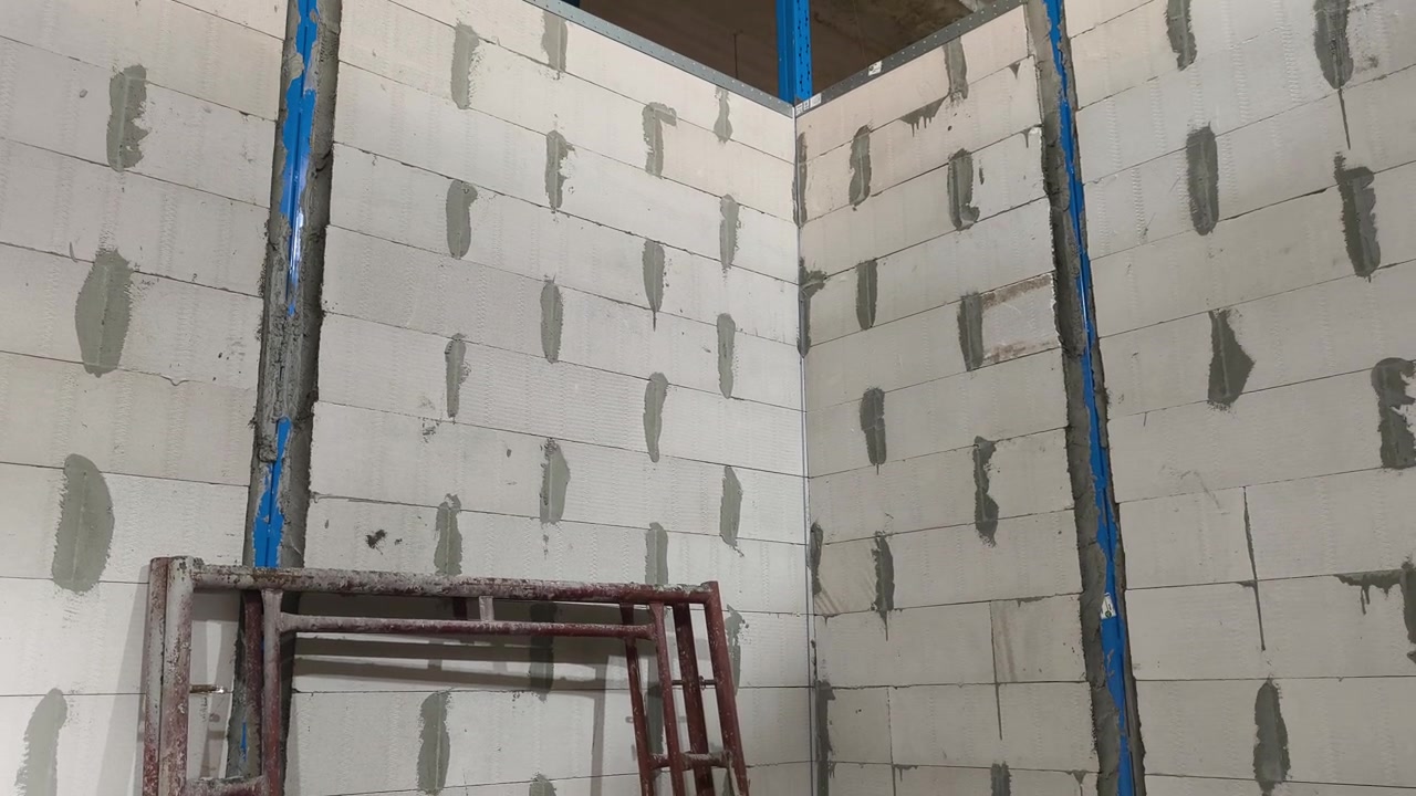 Instalación de muro de bloques de hormigón celular autoclavado (HCA) en una obra de construcción. Incorpora refuerzos metálicos y dinteles para eficiencia estructural. Las técnicas modernas de mampostería aceleran el progreso de la construcción