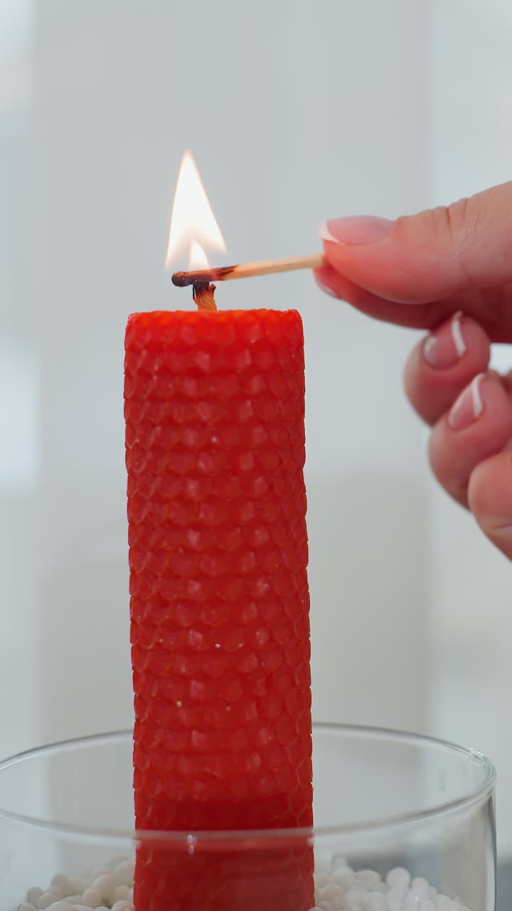 primer plano de mano elegante encendiendo una vela roja con cerilla, creando un ambiente cálido, candelabro de vidrio con cuentas decorativas, mantequilla en el plato y libro en el fondo