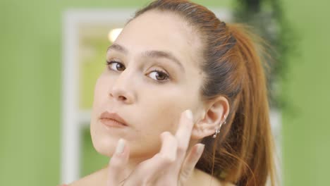 mujer joven aplicando cuidado a la piel de su rostro.