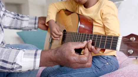 feliz abuelo afroamericano y nieto tocando la guitarra juntos en casa, cámara lenta