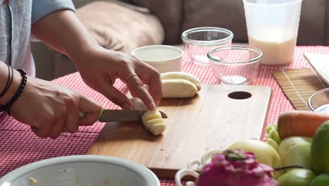 young woman hands cutting banana into slices with knife for preparing healthy fresh juice