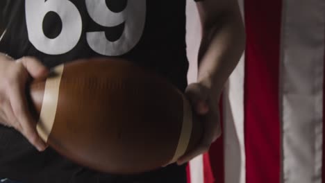 Nahaufnahme-Eines-American-Football-Spielers,-Der-Den-Ball-Gegen-Die-Stars-And-Stripes-Flagge-Im-Hintergrund-Hält